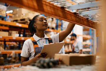 Poster - Black female worker checking inventory on shelves of distribution warehouse.