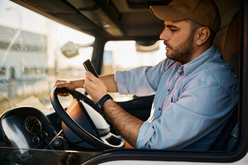 Truck driver reads text message on smart phone while driving transport vehicle.