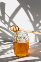 Glass jar with raw honey from bees with honey drops and honey spoon