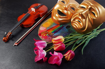 Wall Mural -  Attributes of the arts. Music, painting, theater. Violin, art palette, brushes, theatrical masks and a bouquet of tulips. On a black background.