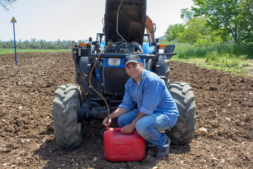 Photo of a farmer sucking diesel oil from a tractor tank with a rubber hose in the middle. Reference to expensive fuel in the agricultural sector