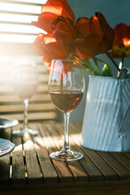 Two Glasses Of Red Wine And A Vase Of Tulips On Dining Table In Sunlight