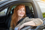 Fototapeta  - Beautiful young woman driving her new car at sunset. Woman in car. Close up portrait of pleasant looking female with glad positive expression, woman in casual wear driving a car