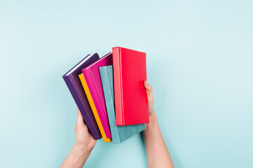 Female hands holding pile of books over light blue background. Education, self-learning, hobby, relax time at home