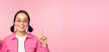 Close Up Portrait Of Modern Korean Female Model, Wears Sunglasses, Points Fingers Up, Shows Advertisement, Promo Banner, Pink Background