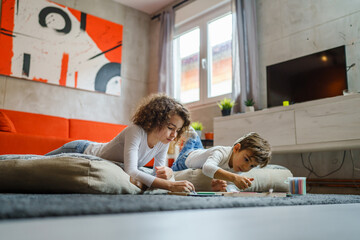 small boy and girl drawing on the green board at home two children brother and sister siblings or friends lying on the floor using chalk leisure and education real people family concept copy space