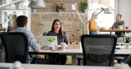 Wall Mural - A group of diverse colleagues clapping for their excited coworker. A cheerful businesswoman working on her laptop, removing her earphones to celebrate her success. Corporate business team celebrating