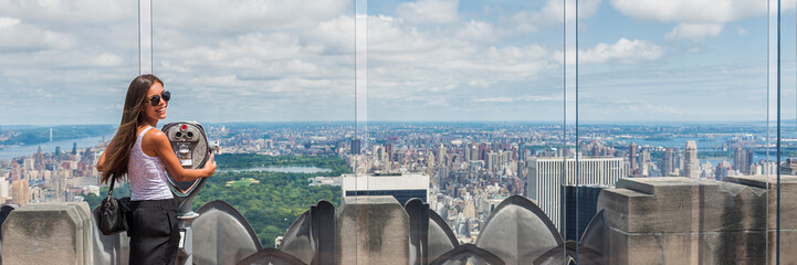 USA travel tourist in New York City vacation- woman looking at view of skyline with binoculars from skyscraper. Girl traveling summer holidays United States road trip