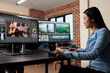 Asian professional video editor sitting at multi monitor workspace while enhancing movie footage quality using advanced software. Post production house team leader editing film frames.