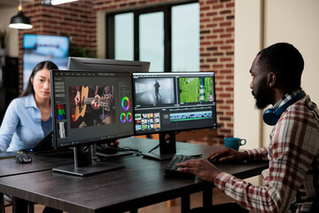 Wall Mural - Creative professional videographer in office sitting at multi monitor workstation while editing digital footage. Post production department visual editor improving video quality.