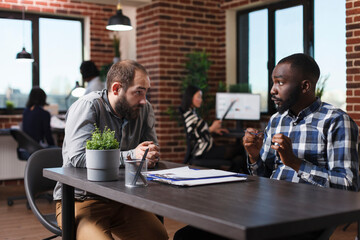 Wall Mural - Young adult african american business company recruiter in process of interview with unemployed man. Job candidate listening to employer talking about job description and salary offer.