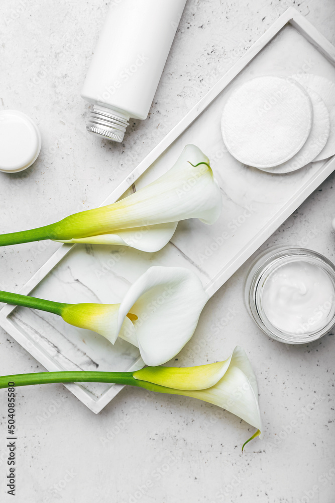 Composition with cosmetic products, cotton pads and calla lilies on light background