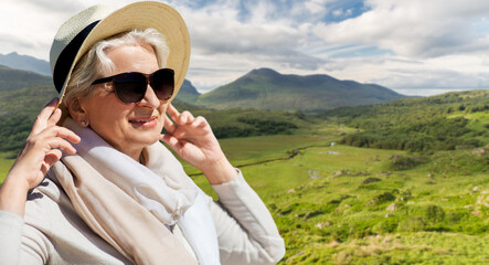 Sticker - travel, tourism and vacation concept - portrait of happy senior woman in sunglasses and straw hat over Killarney National Park valley in ireland background