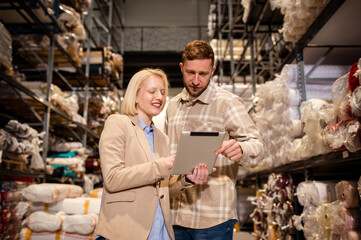 Two business people checking the list and inventory on a tablet. Businesswoman sharing the stock details with warehouse manager.