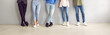 Banner shot of legs of young unrecognizable stylish people in smart and casual clothes. Cropped image of legs of five fashionable men and women standing in row near gray wall. Low section.