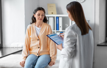 medicine, healthcare and people concept - female doctor with clipboard talking to woman patient at hospital