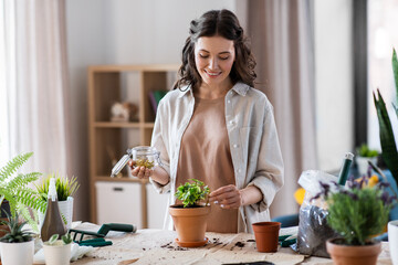 Wall Mural - people, gardening and housework concept - happy woman with fertilizing spikes in jar planting pot flowers at home