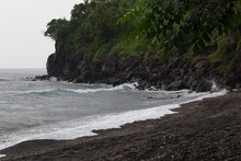 Tropical Beach On Storm - Cape With Black Rocks, Lush Green Forest And   Grey Waves Of Sea With Foam In Rain.  Trip In Rain Season On Bali.