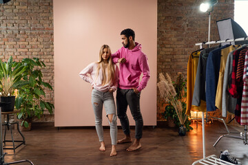 Wall Mural - Fashion studio portrait of a happy young couple in hoodie posing over pink background.