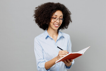 Wall Mural - Young smiling employee business corporate lawyer woman of African American ethnicity in classic formal shirt work in office hold in hand diary notebook writing down notes isolated on grey background.