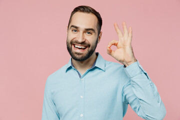 Young smiling satisfied cheerful fun cool caucasian man 20s wearing classic blue shirt showing okay ok gesture isolated on plain pastel light pink background studio portrait. People lifestyle concept.