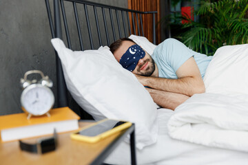 Wall Mural - Young happy man wear casual blue t-shirt blindfold mask on eyes lying in bed hands folded under head rest relax spend time in bedroom lounge home in own room house wake up dream. Real estate concept.