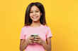 © ViDi Studio - Little smiling kid girl of African American ethnicity 12-13 year old in pink t-shirt hold in hand use mobile cell phone isolated on plain yellow background studio portrait Childhood lifestyle concept