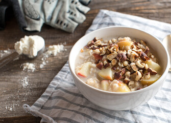 Protein breakfast bowl with porridge. Cooked with whey protein powder and apples. Served with roasted hazelnuts