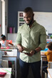 Smiling african american young male teacher with digital tablet standing by multiracial students