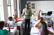 canvas print picture - African american young male teacher with file standing by multiracial students with hand raised