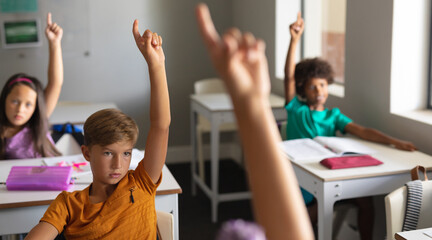  Multiracial elementary school students raising hands during class in classroom