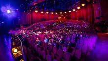 Spectators gather in the auditorium and watch the show in theatre timelapse. Large hall with red armchairs seats. Viewers filling places until turn off the light. View from a stage