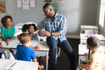 Multiracial elementary students looking at multiracial young male teacher explaining brain model