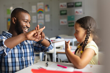 Smiling african american young male teacher teaching sign language to caucasian elementary girl