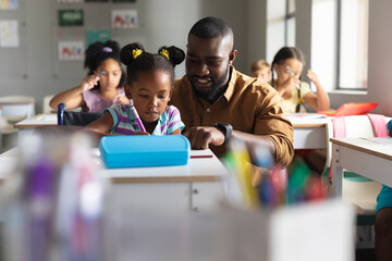 African american young male teacher teaching african american elementary girl on wheelchair in class