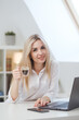 © spaskov - Young beautiful caucasian blonde woman working on laptop at home and drinking coffee. Remote work or freelance.