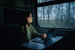 © bodnarphoto - beautiful woman in headphones rides in the evening on the train and works on the computer at the table and looks out the window.