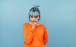 © bodnarphoto - Pensive hipster girl with blue hair and in an orange sweater stands on a blue background and looks at the camera and thinks.
