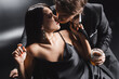 Sexy couple in formal war holding whiskey and kissing on couch on black background.