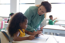 Smiling Caucasian Young Female Teacher Teaching African American Elementary Girl At Desk