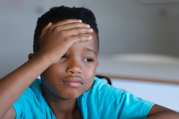 Close-up of sad african american elementary schoolboy with head in hand sitting at desk in class