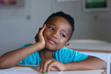 Close-up of african american elementary schoolboy looking away while leaning at desk in classroom