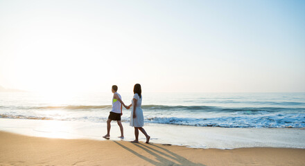 Wall Mural - Young couple holding hand walking on beach.