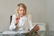 © JENOCHE - senior woman reading newspaper at home