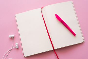 Wall Mural - top view of open notebook and pen near wired earphones on pink.