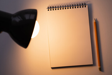 Wall Mural - top view of blank notebook near pencil and turned on lamp on white.