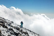 © almostfuture - Climber tourist hikes on frozen rocks and stones over clouds in big mountains