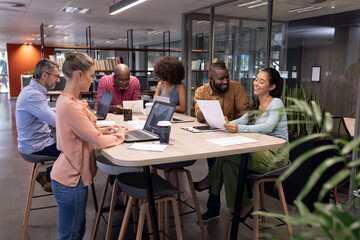 Multiracial male and female professionals working while using technologies and discussing at table