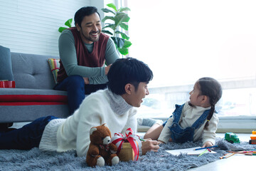 Male gay couple having fun with their daughter at home, lying on the floor, LGBTQ family concept