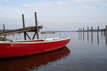 Red And White Rowing Boat Roped Up At The Wooden Pier On A Morning With A Cloudy Sky